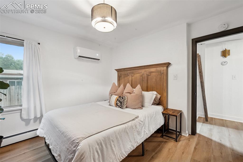 Image 24 of 48: Bedroom with a baseboard heating unit, light wood-style floors, and a wall