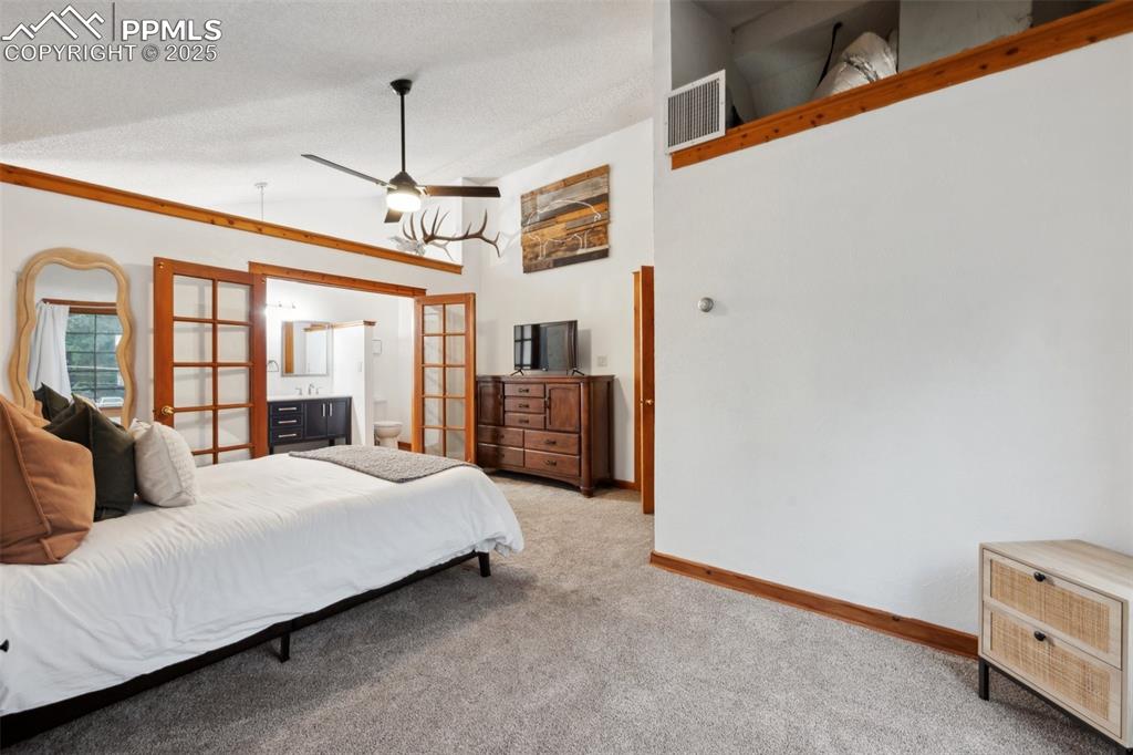 Image 27 of 48: Bedroom with french doors, carpet flooring, vaulted ceiling, a textured cei