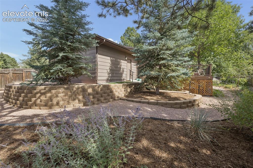 Image 30 of 36: Backyard featuring a stone-retaining wall, gravel pathway, mature trees, ti