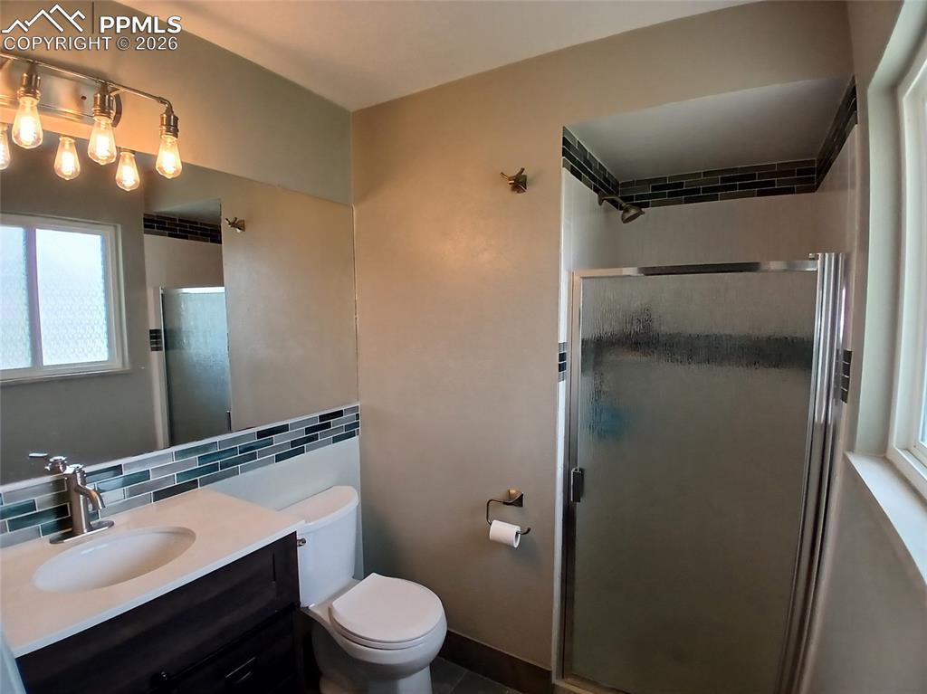 Image 24 of 49: Bathroom featuring tile walls, backsplash, a shower with door, vanity, and 