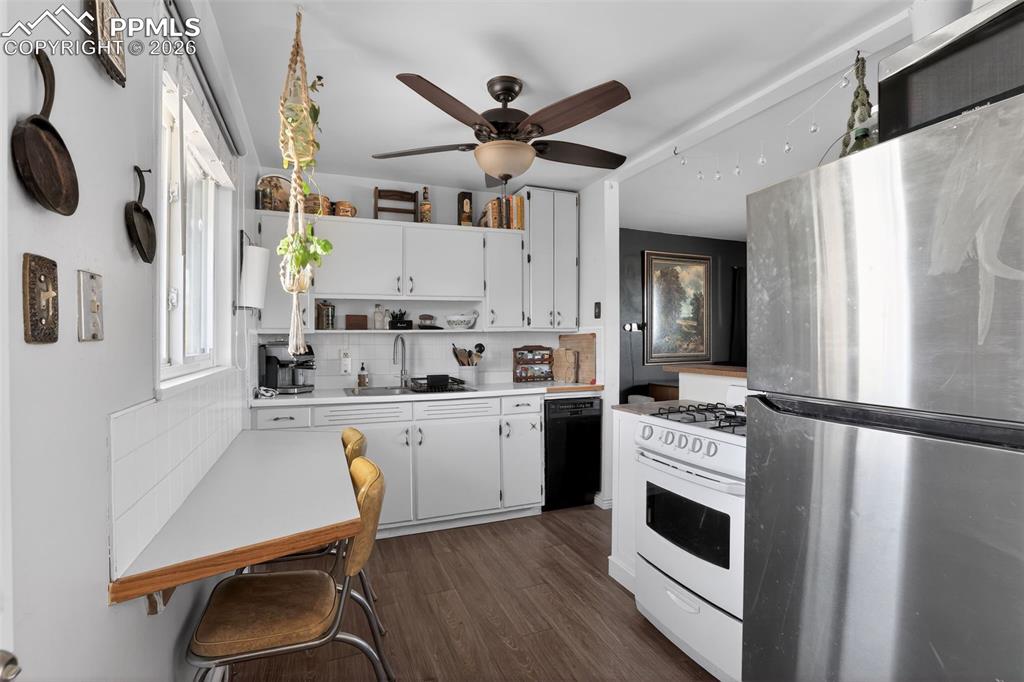 Image 10 of 15: Kitchen with freestanding refrigerator, light countertops, white cabinets,