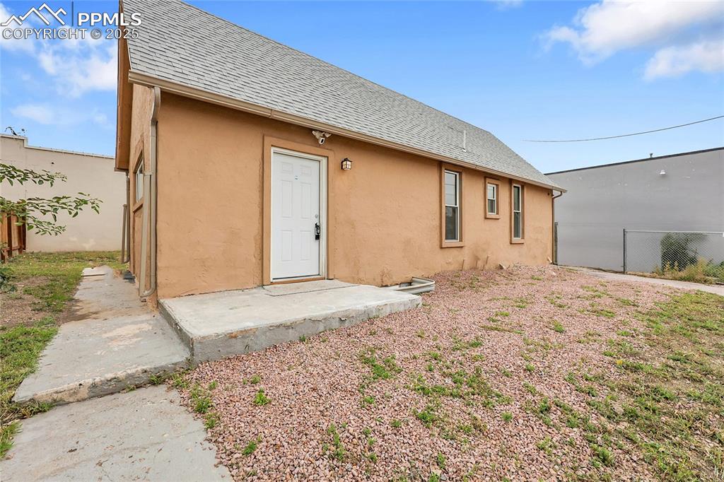 Caption: Back of property featuring a shingled roof and stucco siding