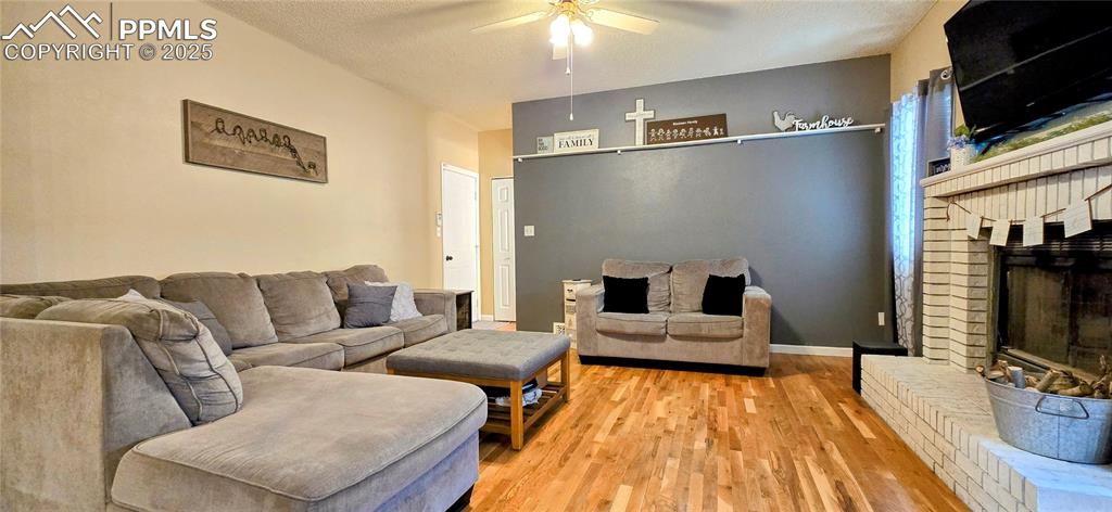 Image 18 of 48: Living area with wood finished floors, a fireplace, a ceiling fan, and a te