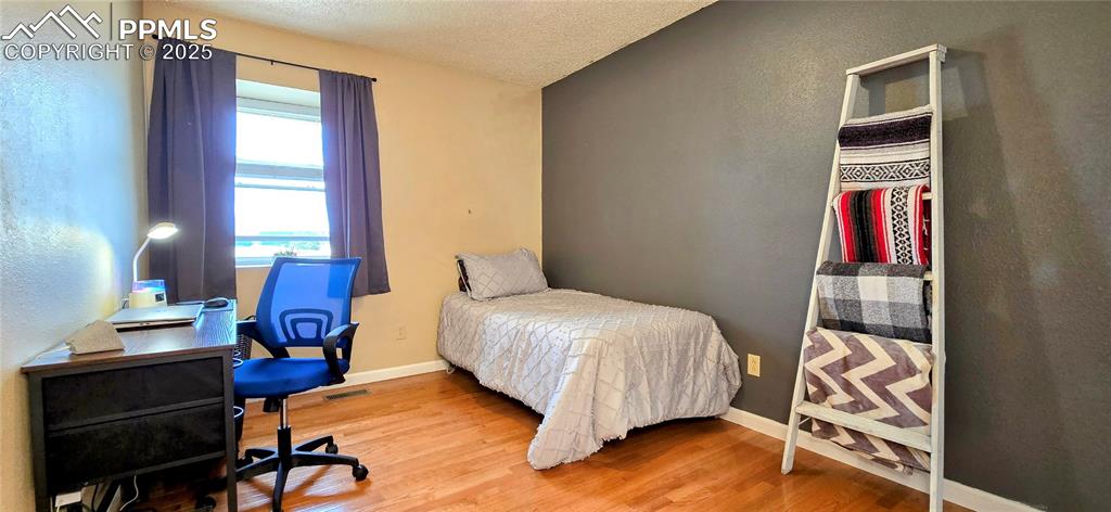 Image 34 of 48: Bedroom featuring wood finished floors, a desk, a textured ceiling, and a t