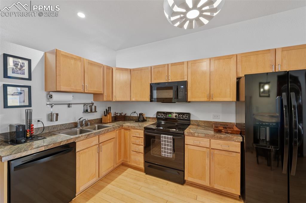Image 14 of 26: Kitchen with light brown cabinetry, light wood finished floors, black appli