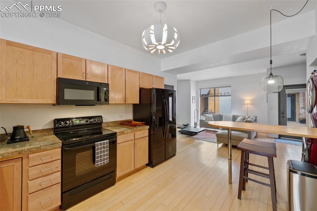 Image 15 of 26: Kitchen with light brown cabinets, black appliances, light wood-style floor