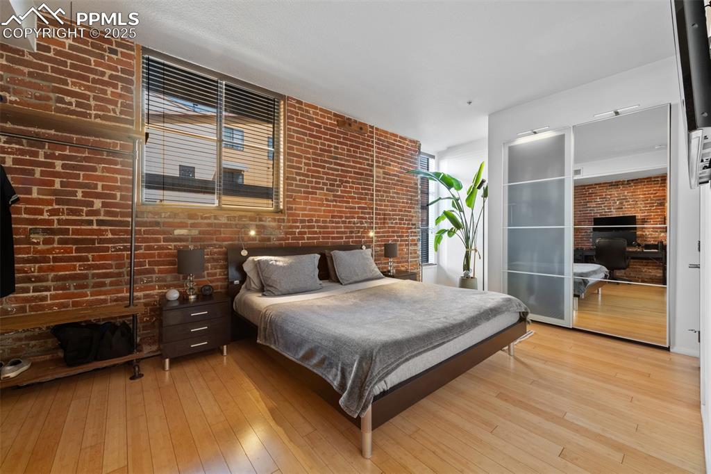 Image 17 of 26: Bedroom featuring brick wall and wood-type flooring