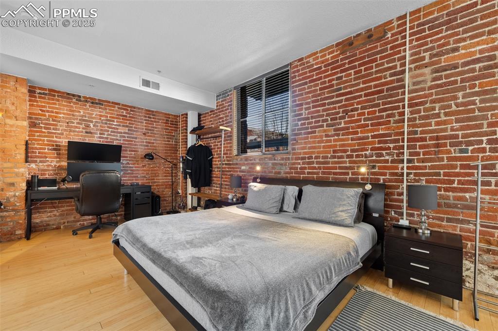 Image 18 of 26: Bedroom with visible vents, brick wall, and hardwood / wood-style floors