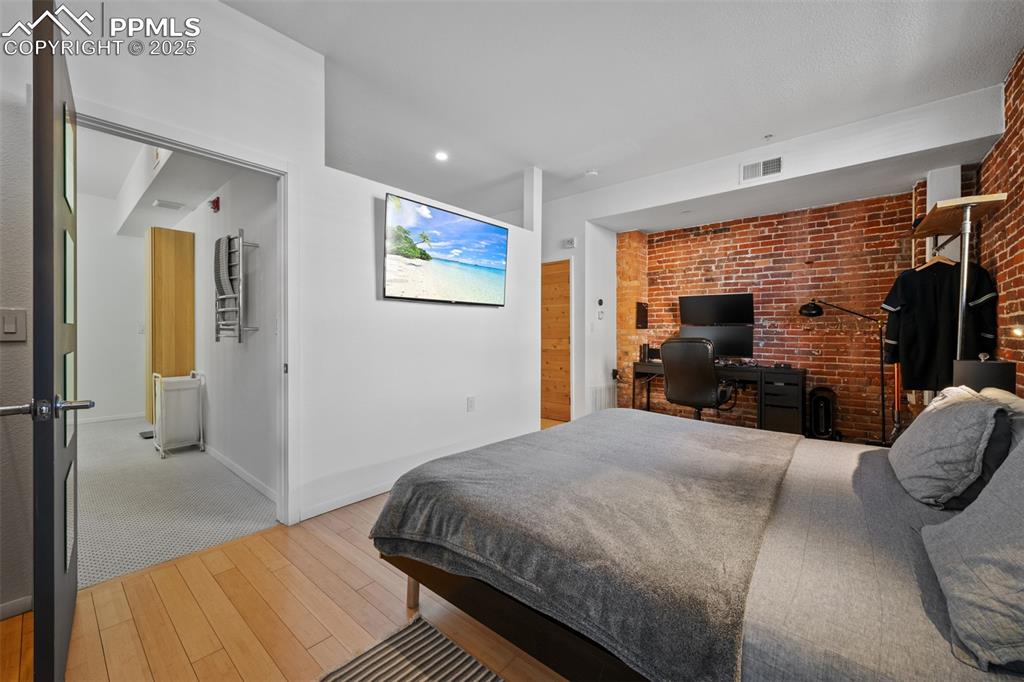 Image 19 of 26: Bedroom featuring wood finished floors, visible vents, brick wall, and base