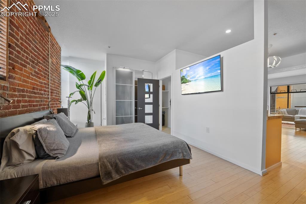 Image 20 of 26: Bedroom featuring baseboards, light wood-style floors, and brick wall