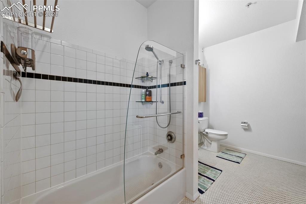 Image 21 of 26: Bathroom with shower / bathing tub combination, toilet, baseboards, and til