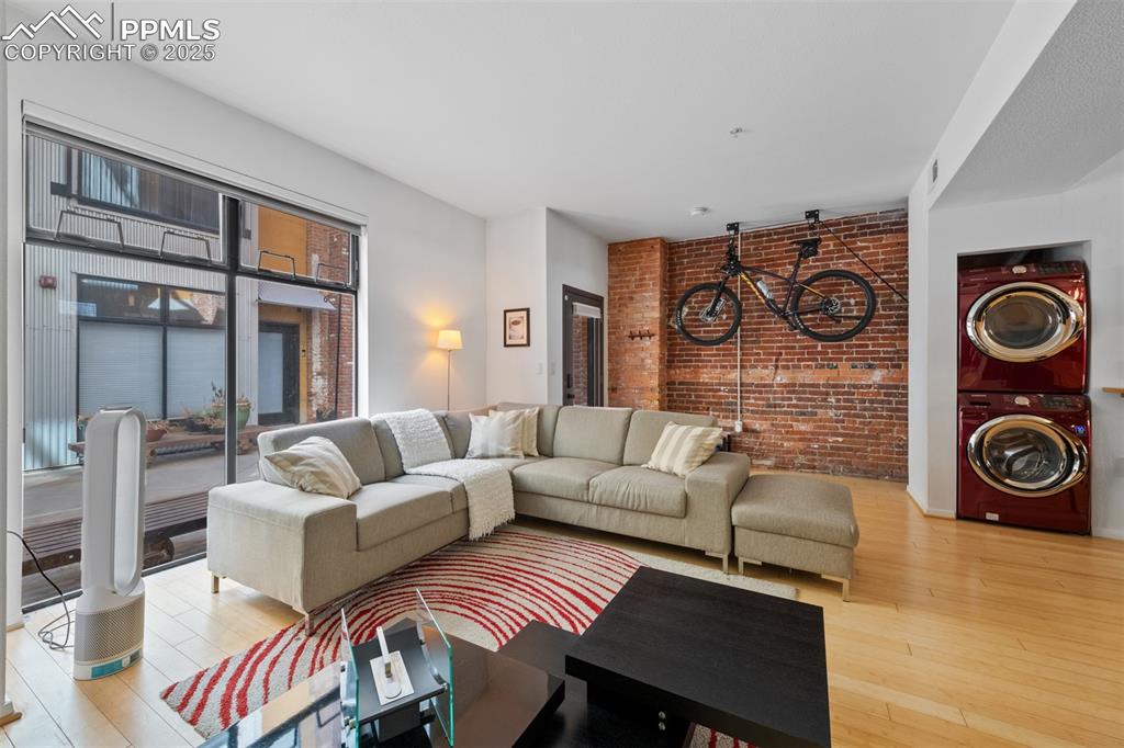 Image 8 of 26: Living area with stacked washer and clothes dryer, brick wall, and hardwood