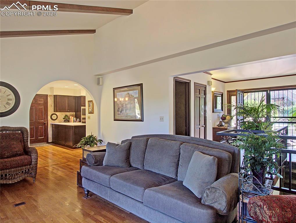 Image 10 of 41: Living area with light wood-style flooring, beam ceiling, and arched walkwa