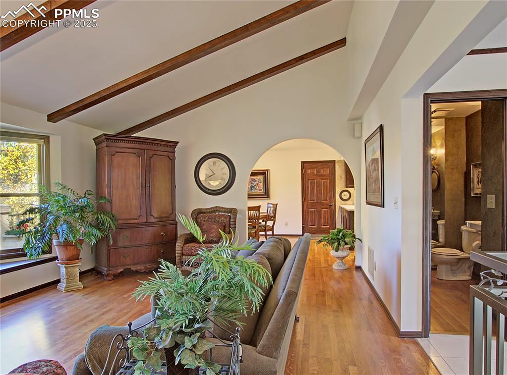 Image 7 of 41: Living area featuring light wood-style floors, arched walkways, beam ceilin