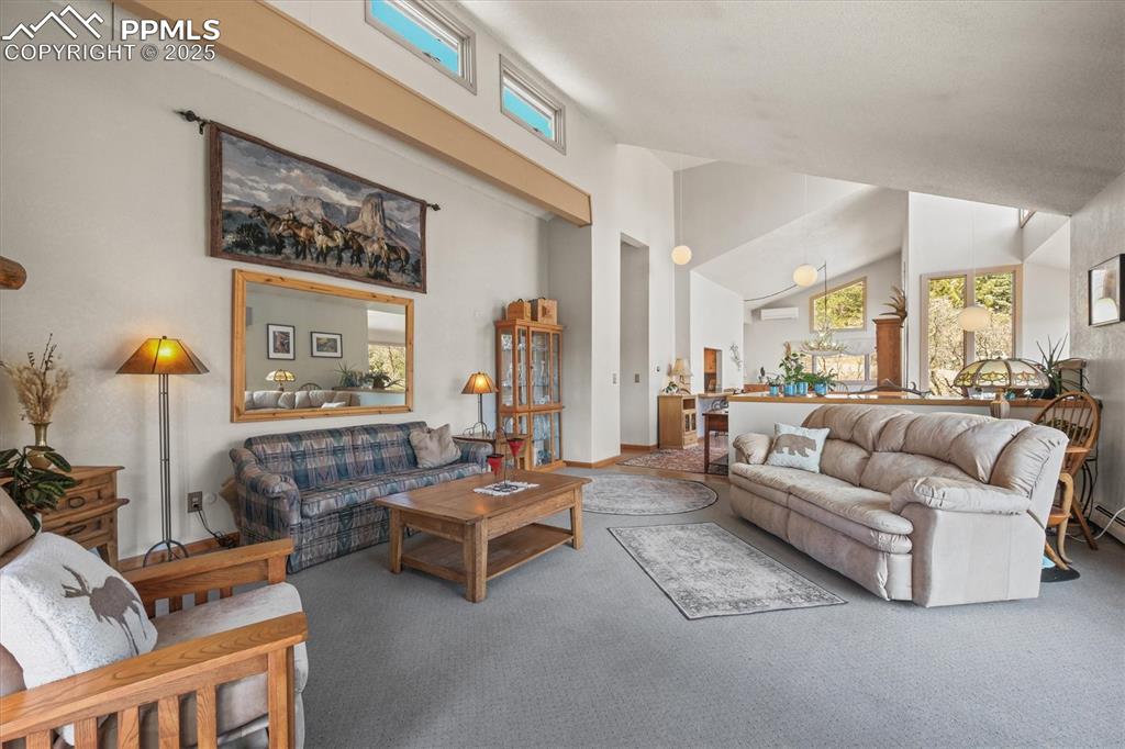Image 10 of 49: Living area with a wall mounted AC, carpet floors, and high vaulted ceiling