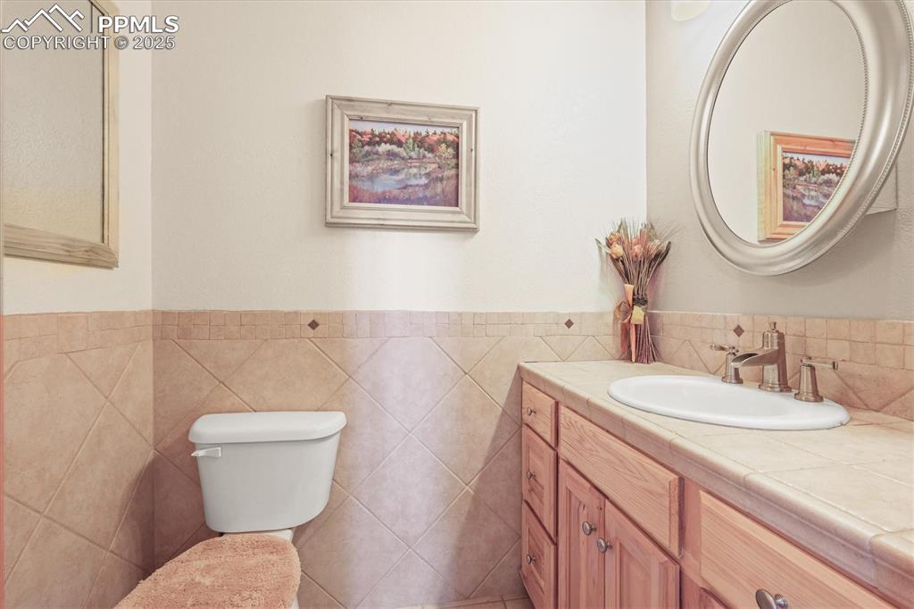 Image 20 of 49: Half bath with toilet, vanity, and tile walls