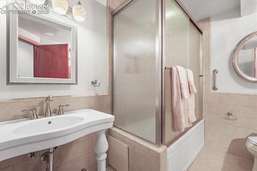 Image 34 of 49: Bathroom with wainscoting, a shower with shower door, tile walls, toilet, a
