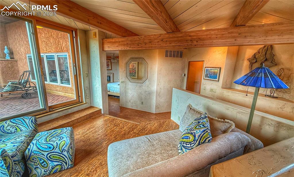 Image 9 of 20: Living area with beam ceiling, and hardwood floor. Slider out to wonderful 