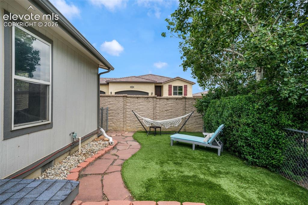 Image 37 of 50: Private backyard featuring artificial turf, a flagstone path, and a raised 