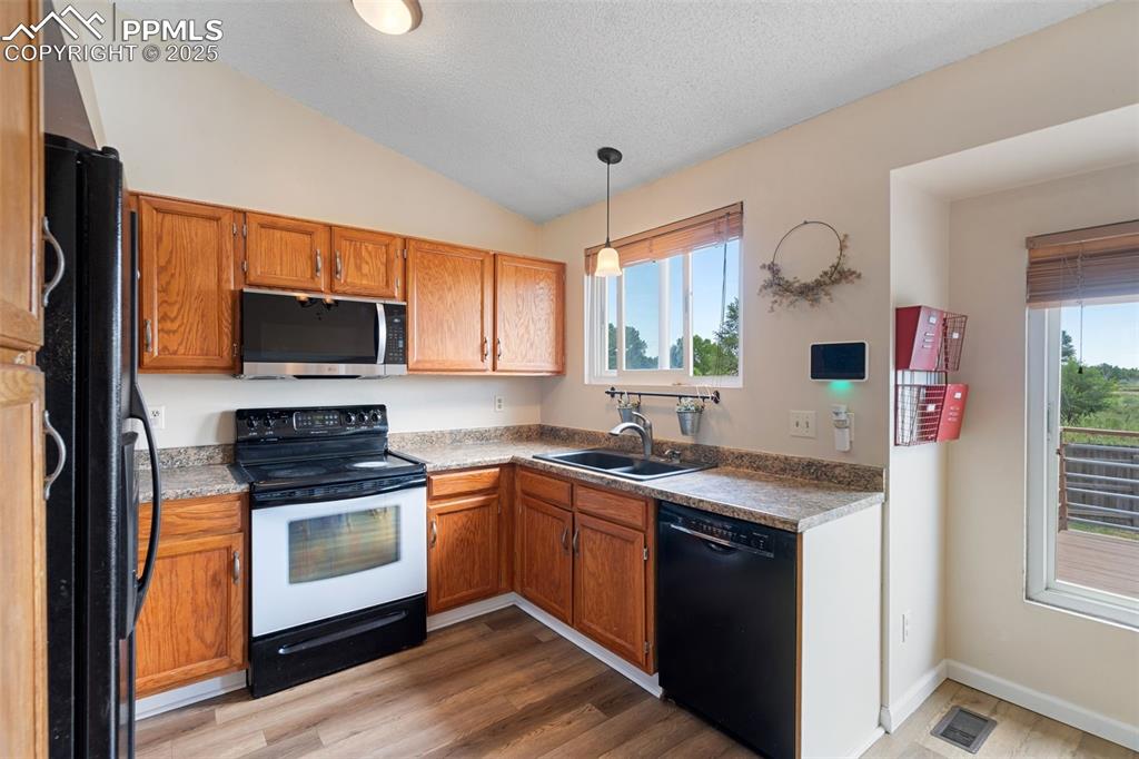 Image 12 of 33: Kitchen featuring black appliances, lofted ceiling, wood finished floors, p