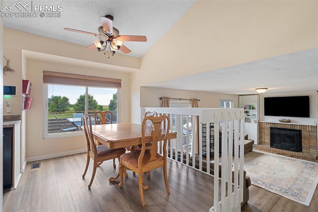 Image 16 of 33: Dining space featuring a fireplace, wood finished floors, ceiling fan, loft