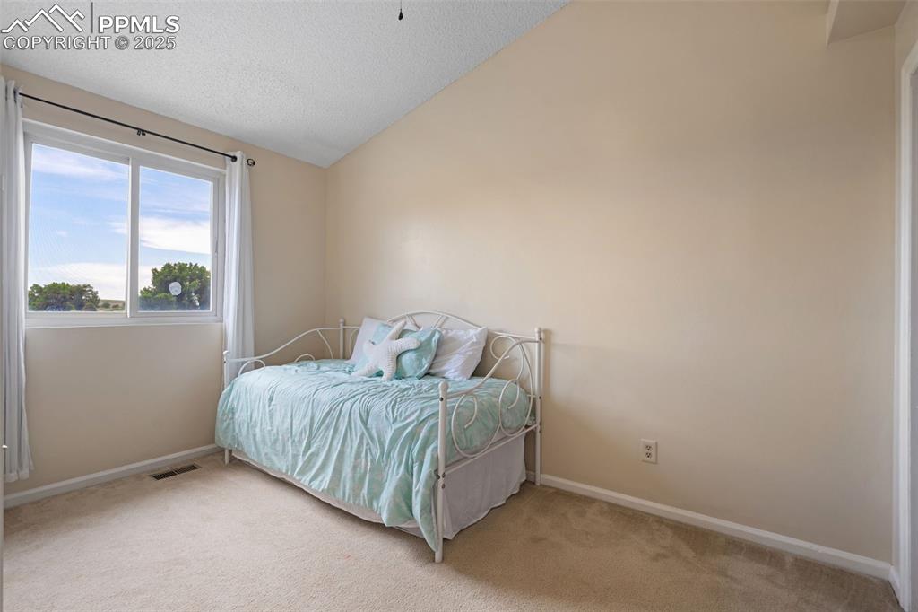 Image 23 of 33: Bedroom featuring light colored carpet, vaulted ceiling, and a textured cei