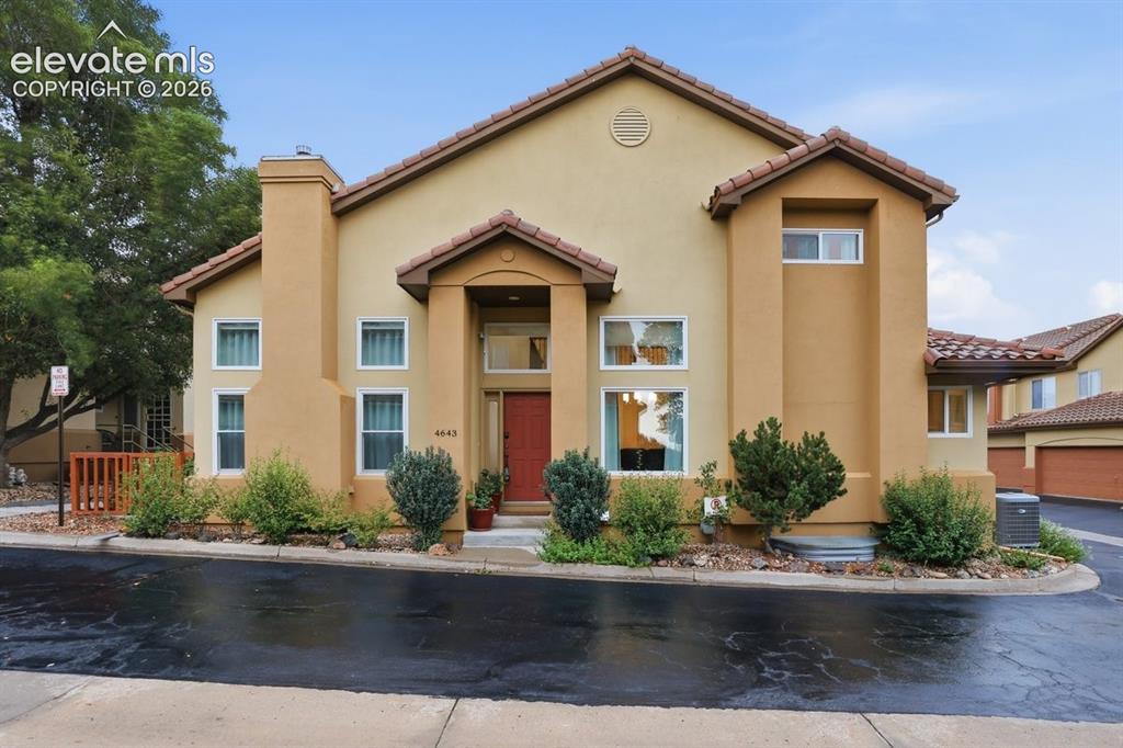 Caption: Stucco exterior featuring a prominent red entry door, multiple large windows, and a tile roof