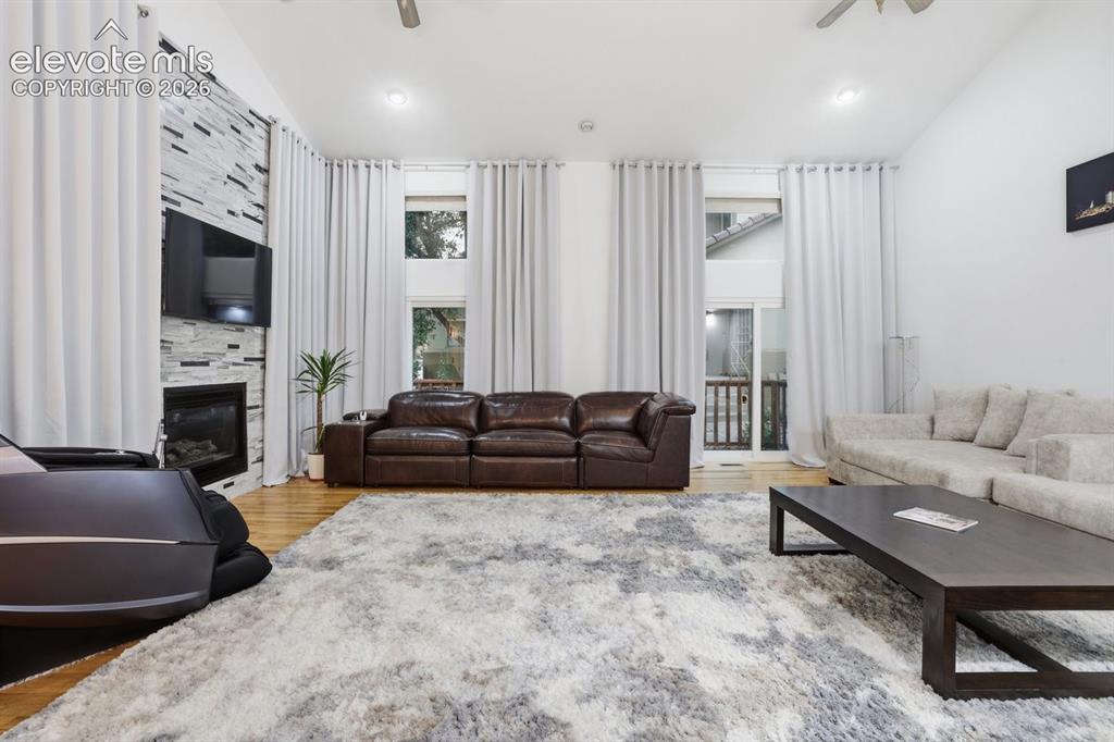 Image 3 of 45: Spacious living area featuring a stone-clad fireplace, hardwood flooring, a