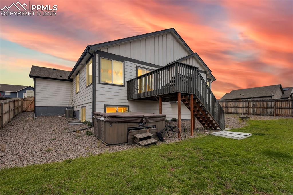 Image 3 of 45: Back of house at dusk with a hot tub, a fenced backyard, a deck, stairs, an