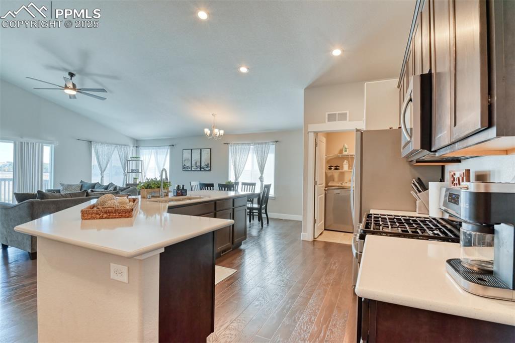 Image 8 of 45: Kitchen with light wood-style floors, dark brown cabinetry, lofted ceiling,