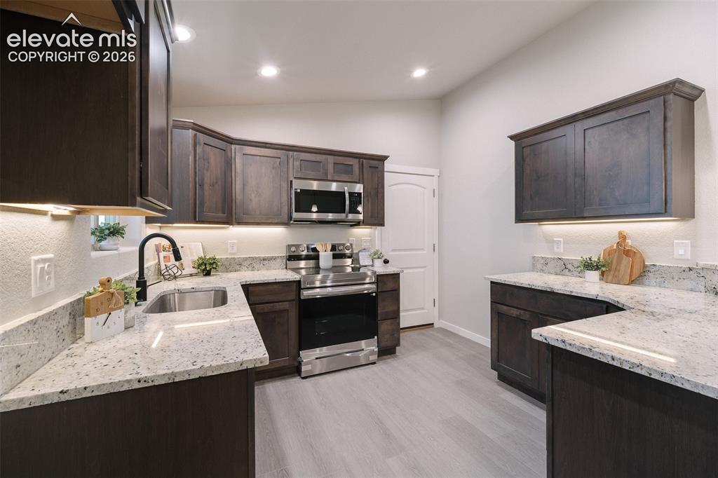 Image 10 of 28: Dark wood-finish cabinetry, stainless steel appliances, light-toned counter
