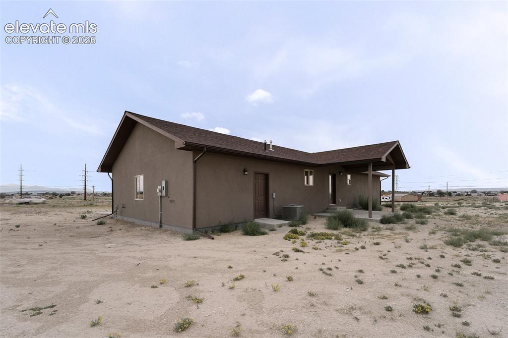 Image 25 of 28: Stucco exterior with a covered entry, brown shingle roofing, and visible do