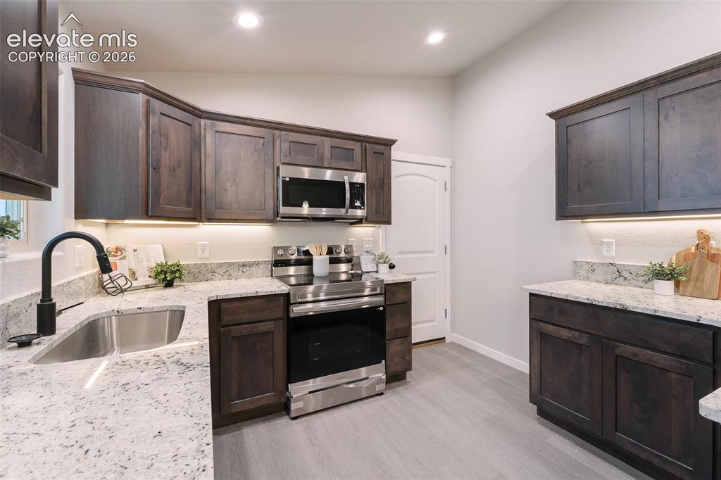 Image 9 of 28: Kitchen featuring dark wood cabinetry, light-toned countertops, stainless s