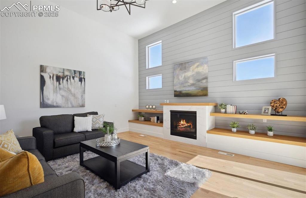 Image 6 of 31: Living area with wood finished floors, a warm lit fireplace, a high ceiling