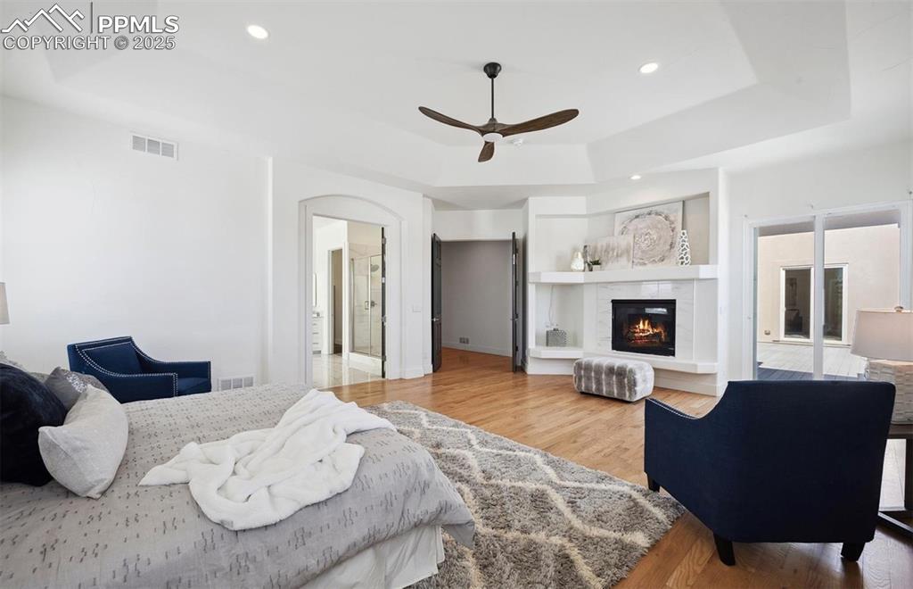Image 7 of 31: Bedroom with a raised ceiling, wood finished floors, ensuite bath, a tiled 