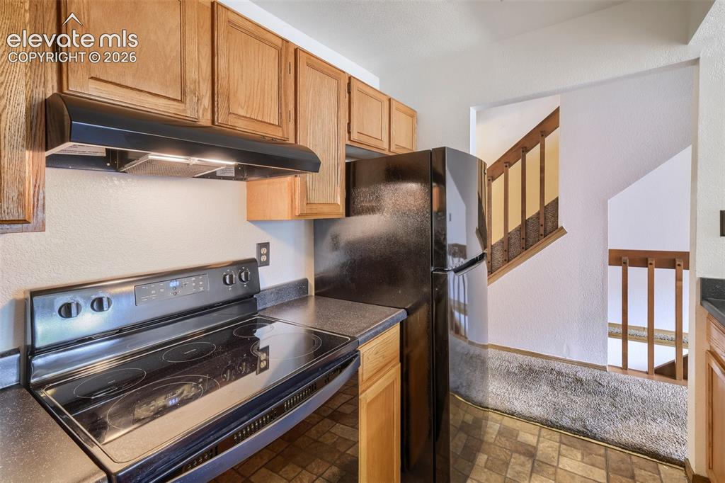 Image 10 of 35: Kitchen featuring wood cabinetry, black electric range with overhead vent,