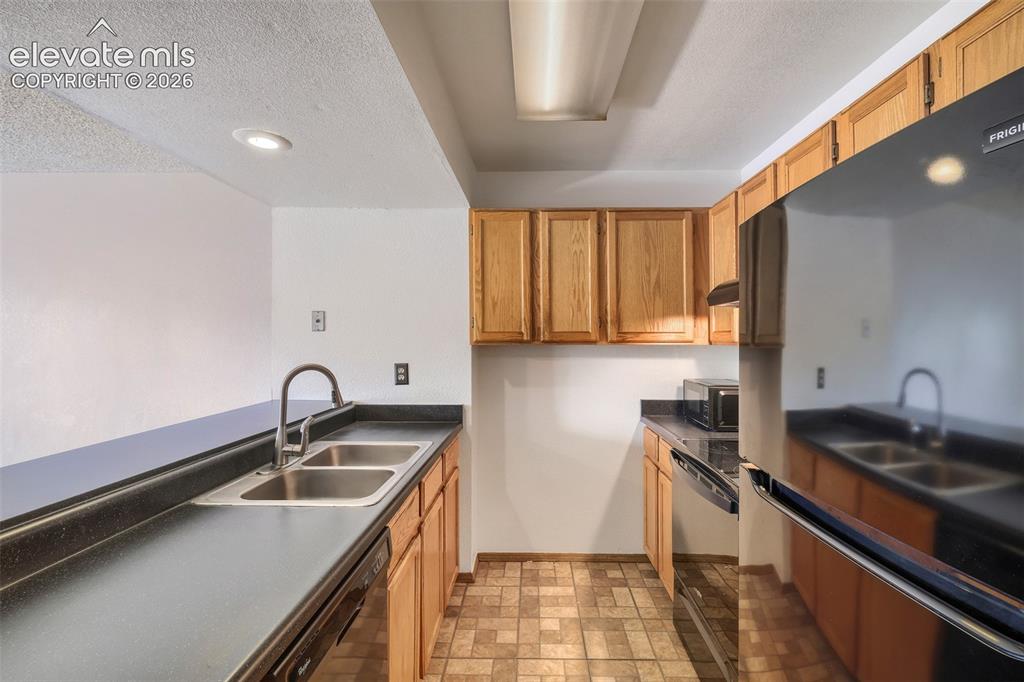 Image 11 of 35: Kitchen featuring wood cabinetry, black countertops, a stainless steel doub
