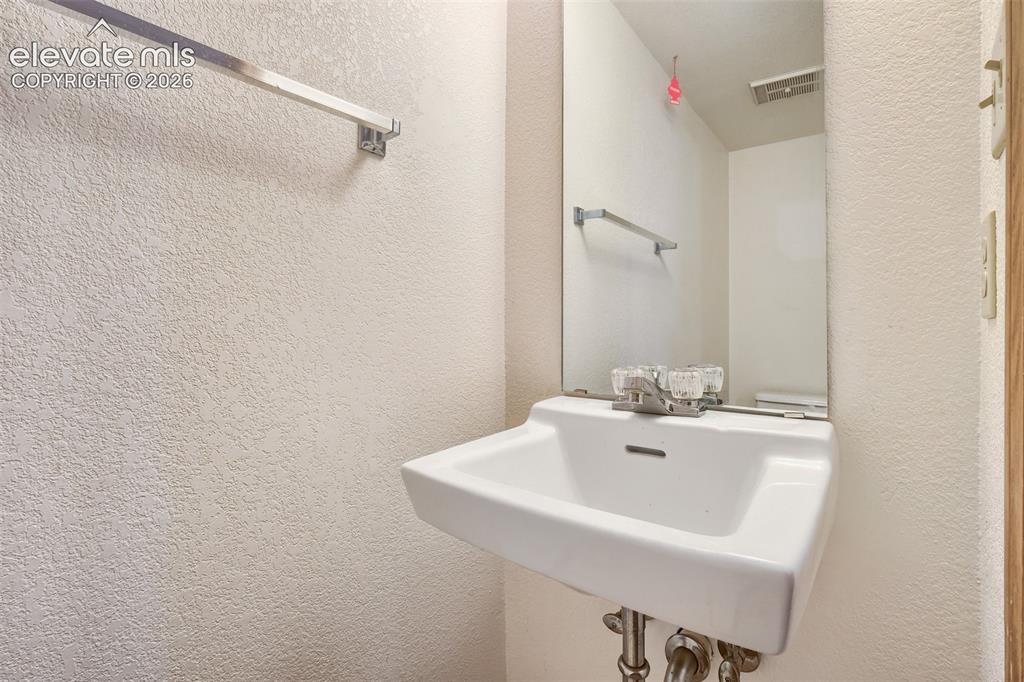 Image 13 of 35: Pedestal sink with chrome faucet set, wall-mounted mirror, and textured wal