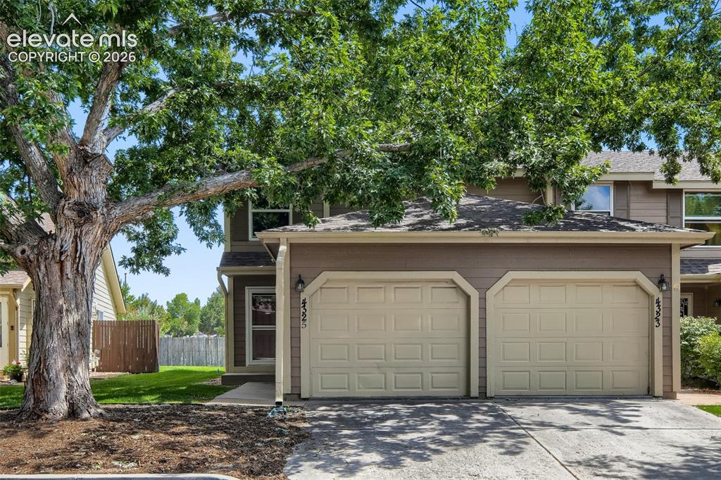 Image 2 of 35: Two-story exterior with earth-toned siding, a two-car garage with paneled d