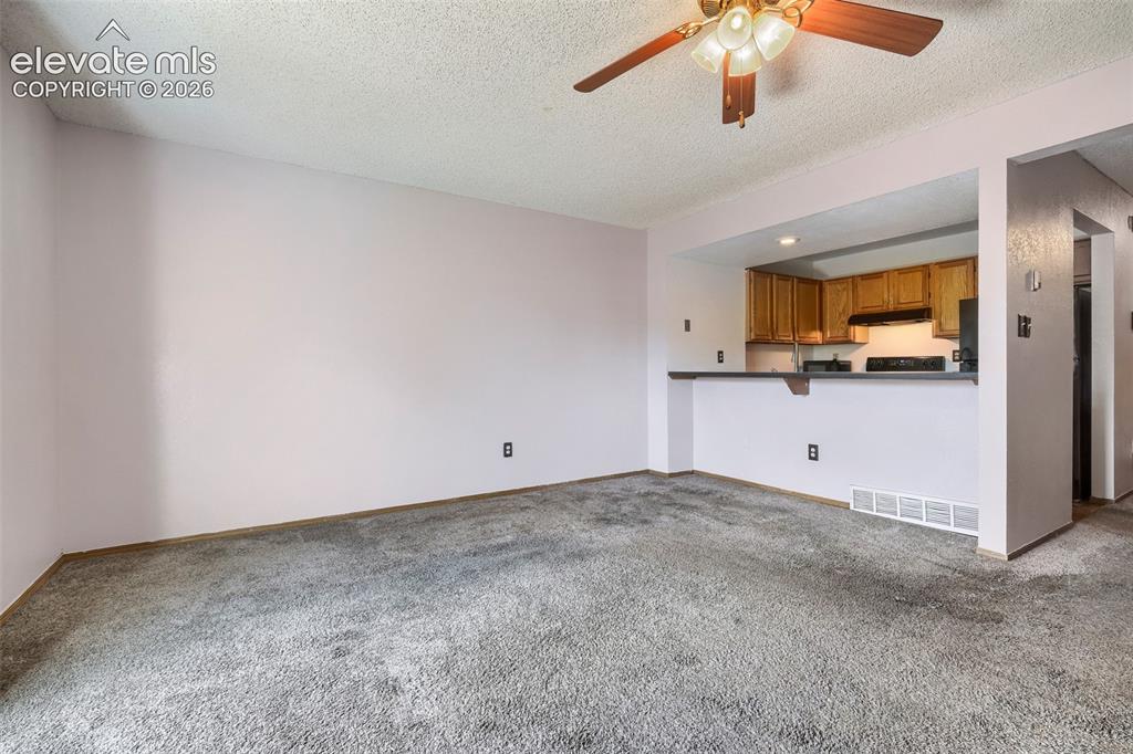 Image 4 of 35: Carpeted living area featuring a pass-through counter to the kitchen, a cei