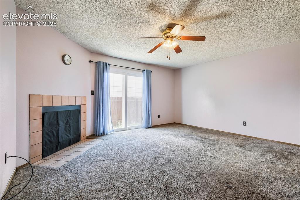 Image 6 of 35: Living area featuring a tiled fireplace with hearth, sliding glass door, te