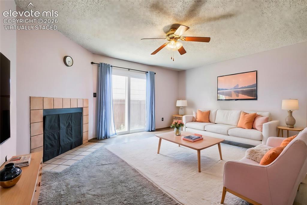Image 7 of 35: Virtually Staged - Living area with a tiled fireplace, ceiling fan, and sli