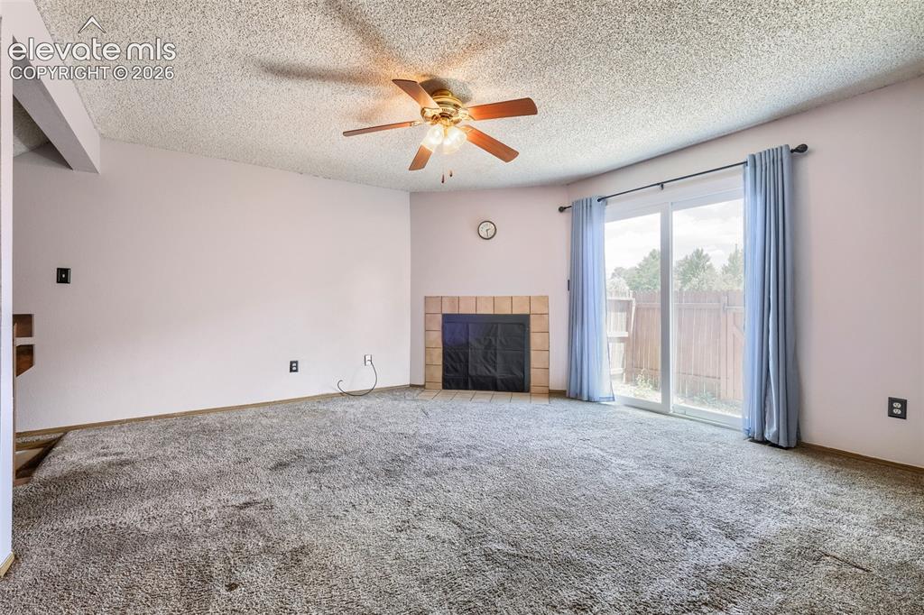 Image 8 of 35: Spacious room featuring a fireplace with a tiled surround, a sliding glass