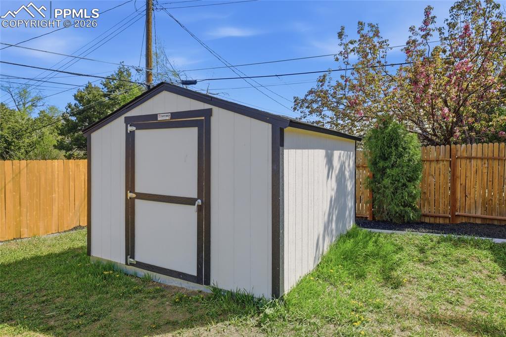 Image 35 of 44: The property features a white shed with dark trim, situated on a lawn