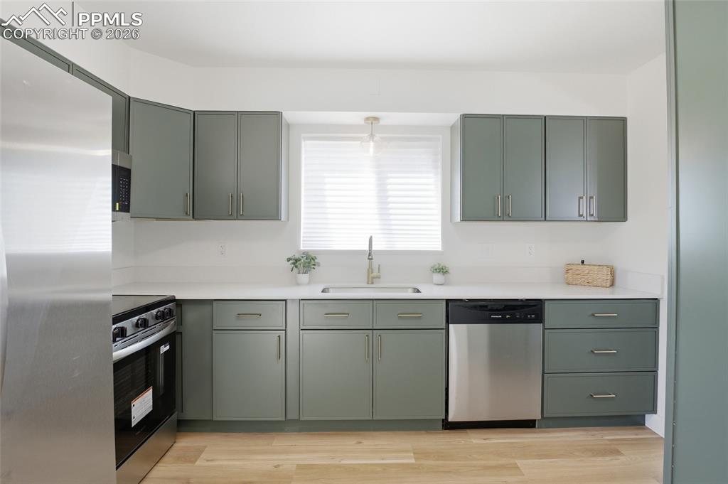 Image 8 of 44: The kitchen features green cabinetry, stainless steel appliances, a window 