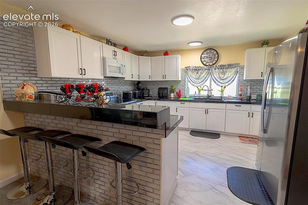 Image 21 of 25: Kitchen with white microwave, freestanding refrigerator, light marble finis