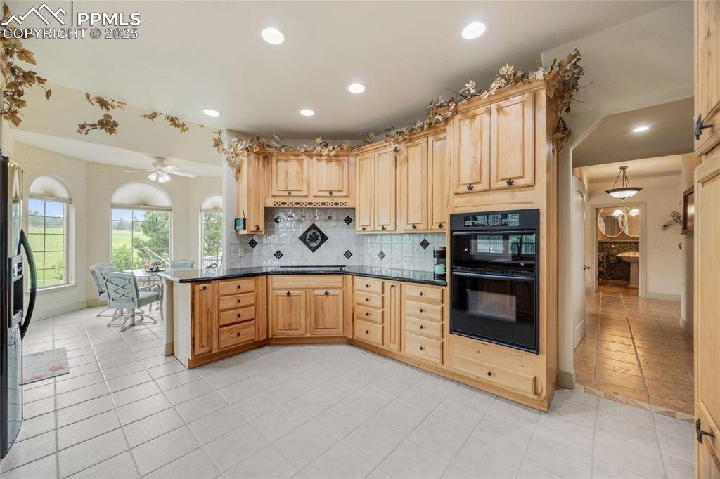 Image 14 of 41: Kitchen with backsplash, dark countertops, recessed lighting, light brown c