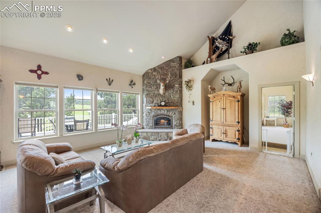 Image 17 of 41: Living room with a stone fireplace, light carpet, high vaulted ceiling, and