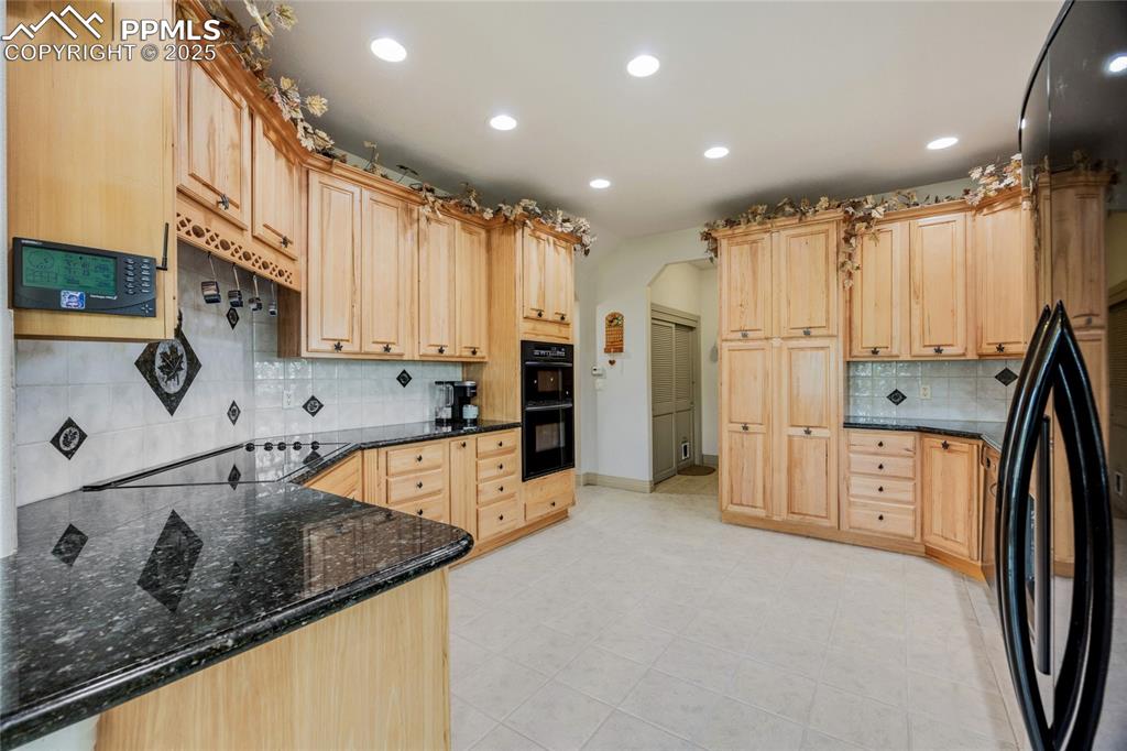Image 19 of 41: Kitchen with black appliances, decorative backsplash, light brown cabinets,