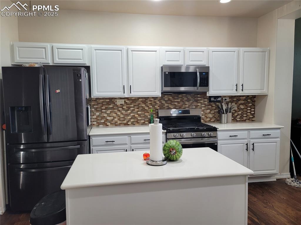 Image 8 of 11: Kitchen with stainless steel appliances, white cabinets, dark wood-style fl